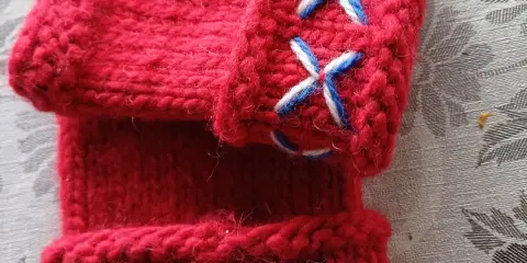 Närbild på röda, stickade vantar utan fingrar med korsstygn i vitt och blått. Perfekt för att virka vantar utan fingrar.