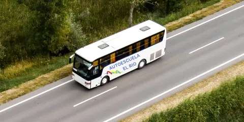 Autobús blanco de la autoescuela El Río en una carretera, preparándose para un examen en la pista.