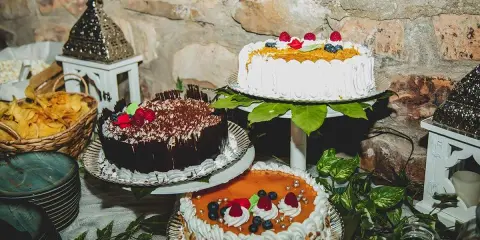 Mesa dulce boda casera con tres pasteles decorados con frutas y chocolate. Hay también cestas con patatas fritas y adornos rústicos.
