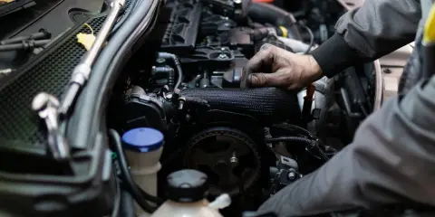 Mechanik pracuje przy silniku benzynowym, jego ręce są ubrudzone smarem.