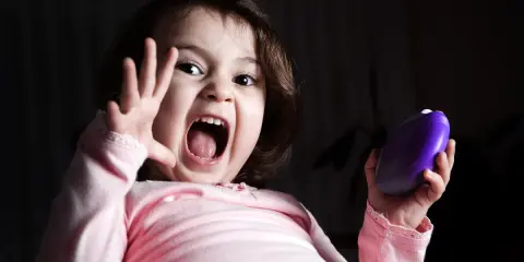 Niño asustado grita con la boca abierta, levantando una mano y sosteniendo un objeto morado.