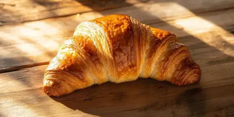 Un délicieux croissant maison, doré et feuilleté, repose sur une table en bois baignée de soleil.