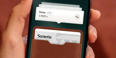 Une main tient un smartphone affichant l'application Sumeria. Une carte bancaire Sumeria est visible dans un étui en cuir marron.