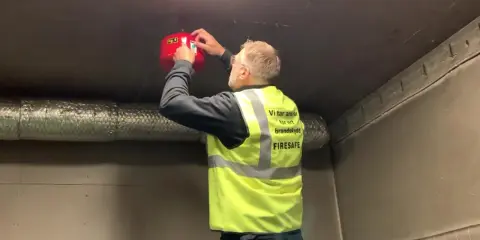 Man i varselväst installerar en brandsläckare i ett utomhus soprum.