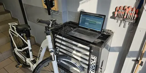 Profesjonalna naprawa rowerów elektrycznych w warsztacie. Biały rower elektryczny, laptop z oprogramowaniem diagnostycznym i zestaw narzędzi.