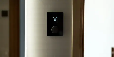 Nowoczesny termostat steruje ogrzewaniem elektrycznym, pokazując temperaturę 27 stopni.