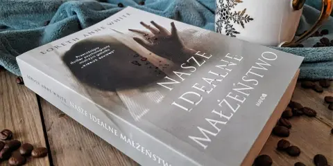 Książka "Nasze idealne małżeństwo" na drewnianym blacie, obok filiżanki i ziaren kawy.