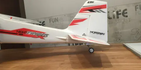 Modellflugzeug mit Aufschrift "NIGHT TIMBER" und "Eflite" Logo. Das Flugzeug steht auf einem Holztisch, bereit zum Flug.