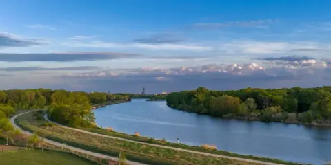 Wisła, jaka rzeka płynie przez Kraków, meandruje wśród zieleni. W oddali widać miejską panoramę.