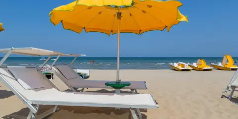 Spiagge di Rimini con lettini, ombrellone giallo e pedalò pronti per l'estate.