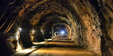 Wąski tunel w kopalni, oświetlony lampami, prowadzi w głąb ziemi. To jedne z wielu tajemniczych jaskiń Dolnego Śląska.