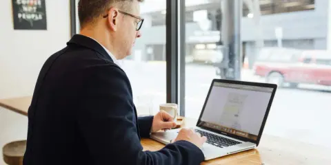 Hombre revisa en su laptop una cotización a tiempo parcial a efectos de jubilación, sentado en una cafetería.