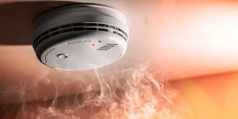 Brandvarnarens dag: en rökdetektor på taket med en röd lampa lyser, omgiven av dramatisk rök och ljus.