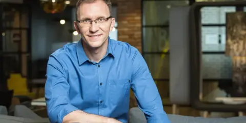 Marcin Iwuć, twórca "Finansowej fortecy", w niebieskiej koszuli siedzi na kanapie, uśmiechając się do obiektywu.