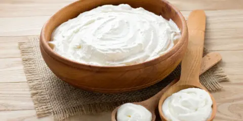 Cremiger Schmand in Holzschale und Löffeln. Ist Schmand gesund? Ja, in Maßen genossen, liefert er Kalzium und Proteine.