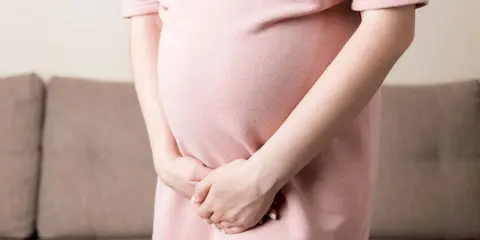 Kobieta w ciąży w różowej sukience trzyma ręce na brzuchu, doświadczając dyskomfortu związanego z nietrzymaniem moczu w ciąży.