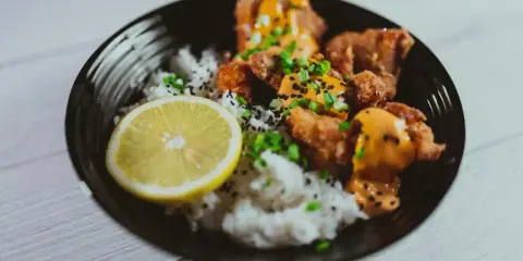 Chrupiące karaage z ryżem, posypane sezamem i szczypiorkiem, podane z plasterkiem cytryny.