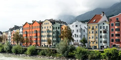 Bunte Häuserzeile am Flussufer, ein Beispiel dafür, was ein Ballungsraum ist: dicht bebaut, mit Bergen im Hintergrund.