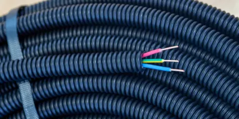 Gaine électrique bleue enroulée, prête pour une installation dans le jardin. Trois fils colorés (rose, jaune, bleu) émergent de son extrémité, suggérant la profondeur de son utilité.