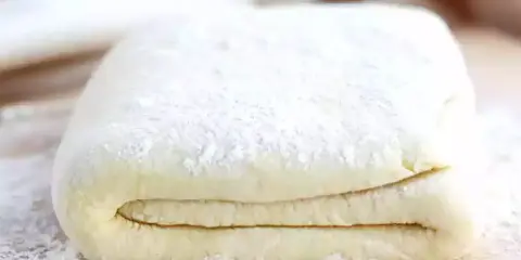 Pâte feuilletée prête à être utilisée pour votre recette. Les couches sont bien visibles, saupoudrées de farine.