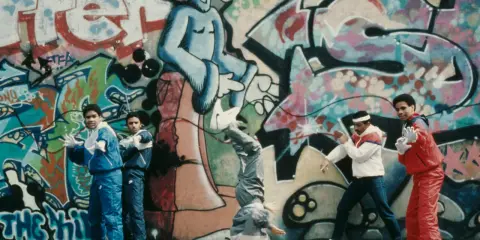A group of young people showcase their moves in front of vibrant graffiti art, embodying the spirit of hip hop culture art.