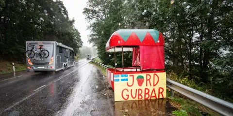 Regnig dag vid vägkanten med en jordgubbsförsäljning. Husbilen passerar, kanske på väg till sommarstugan under fruntimmersveckan, som bondepraktikan säger.