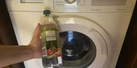Ręka trzyma butelkę octu spirytusowego obok pralki Bosch. To początek domowego sposobu na mycie pralki octem.