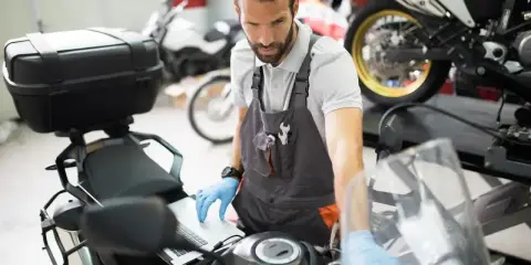 Mechanik w warsztacie sprawdza przegląd motocykla po terminie, używając laptopa do diagnostyki.
