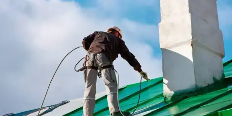 Pracownik na dachu maluje pistoletem zielony dach. Czy Hammerite można malować pistoletem? Tak, można!