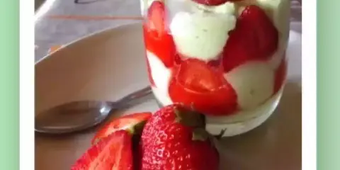 Un délicieux tiramisu pistache fraise, présenté en verrine avec des fraises fraîches sur le côté.
