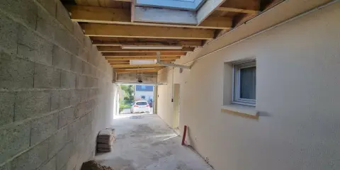 Couloir en construction, partie d'une extension maison, avec murs en parpaings, plafond en bois, fenêtre de toit et matériaux de chantier.