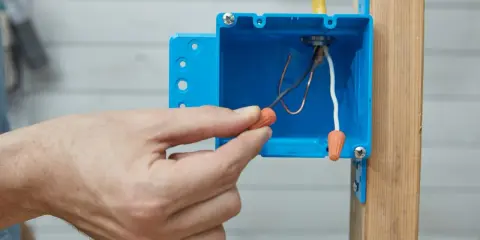 Main tenant utilise un connecteur pour condamner une prise électrique. Les fils électriques sont visibles dans la boîte bleue.