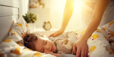 Mama pomaga dziecku zasnąć, kładąc rękę na jego ramieniu. Słodki sen malucha to pierwszy krok, jak nauczyć dziecko zasypiać samo.