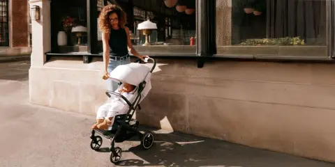 Kobieta prowadzi dziecko w wózku Cybex Beezy ulicą.