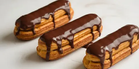 Trois éclairs au chocolat, parfaits pour une recette opera. La ganache dégouline sur la pâte à choux dorée.