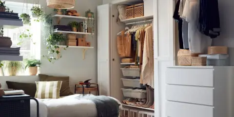Ett inrett litet sovrum med en säng, öppen garderob och hyllor fyllda med växter och förvaring.