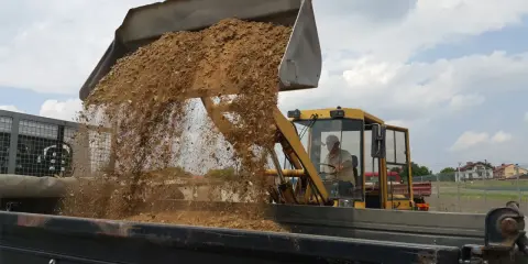 Koparka wysypuje piasek do wywrotki. Zastanawiasz się, ile waży m3 piasku?