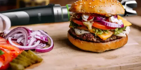 Pyszny burger z serem, warzywami i domowym sosem do burgera. Obok pokrojona cebula i pomidor.