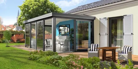 Moderne veranda sans permis de construire, avec table et chaises, offrant une vue sur un jardin verdoyant et des maisons.