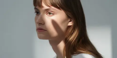 Une jeune femme aux cheveux châtains, une ombre sur le visage, parfaite pour apprendre comment coiffer une frange sur le côté.