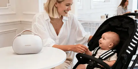 Uśmiechnięta mama z niemowlakiem w wózku, przygotowująca się do sylwestra. Obok biała torba Momcozy.