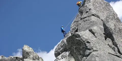 Dwóch wspinaczy pokonuje skalny szczyt Mnich w Tatrach. Jeden z nich zjeżdża na linie, drugi wspina się wyżej.