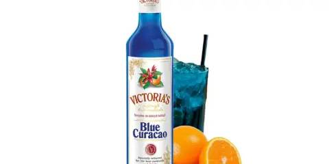 Syrop Blue Curacao Victoria's, idealny do drinków. W szklance niebieski koktajl z lodem i słomką, obok pomarańcze.