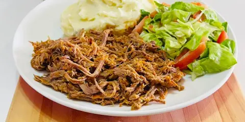 Plato de carne mechada jugosa, puré de papas cremoso y ensalada fresca de lechuga y tomate.