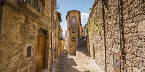 Antica scala di borgo in pietra, con case strette e un cielo azzurro.