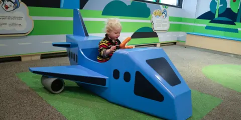 Liten pojke leker i ett blått leksaksplan. En rolig resa med bebis börjar här!