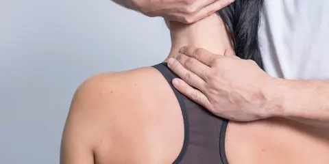 Hände eines Therapeuten untersuchen den Nacken einer Frau, um schmerzen seitlich am Hals entlang zu lindern.