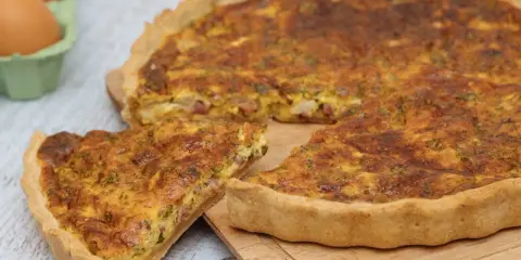 Une part de quiche lorraine dorée, avec sa garniture aux lardons et herbes, prête à être dégustée. La vraie recette quiche lorraine.