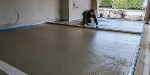 Pracownik wyrównuje świeży beton, tworząc połączenie posadzki garażu z podjazdem.