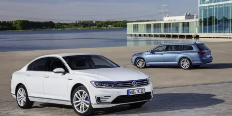Dos coches Volkswagen, uno blanco sedán y otro azul familiar, estacionados frente a un edificio moderno junto a un lago. ¿Cuál es el permiso de coche?